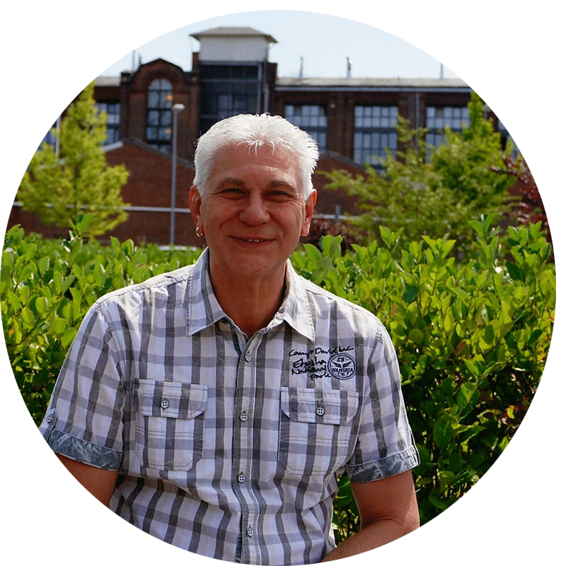 Atila Keckes, der Geschäftsführer von Pat.nrw lächelt nett in die Kamera uns sitzt vor einem grünen Busch